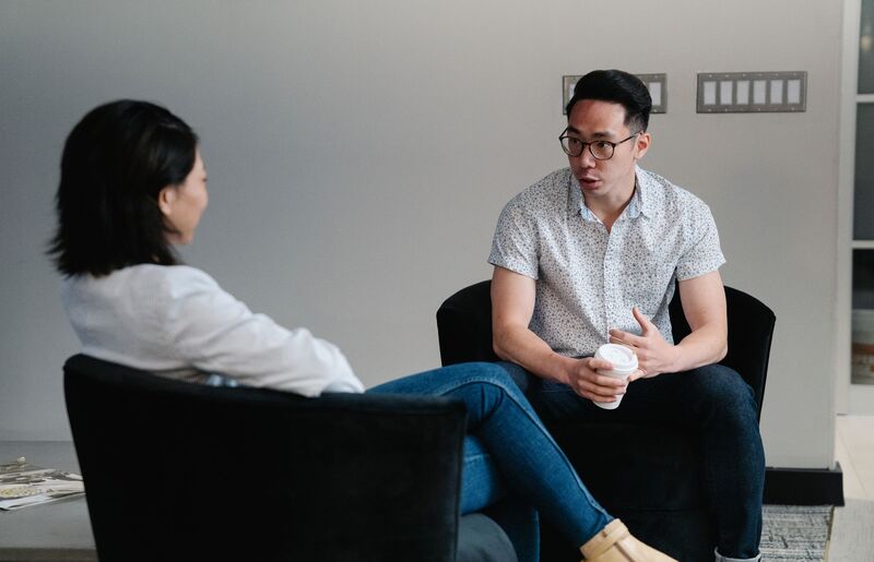 Two people sitting in armchairs having a conversation, one of them holding a coffee cup