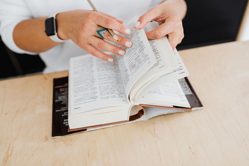 A person at a wooden desk leafing through a dictionary with a pencil in hand